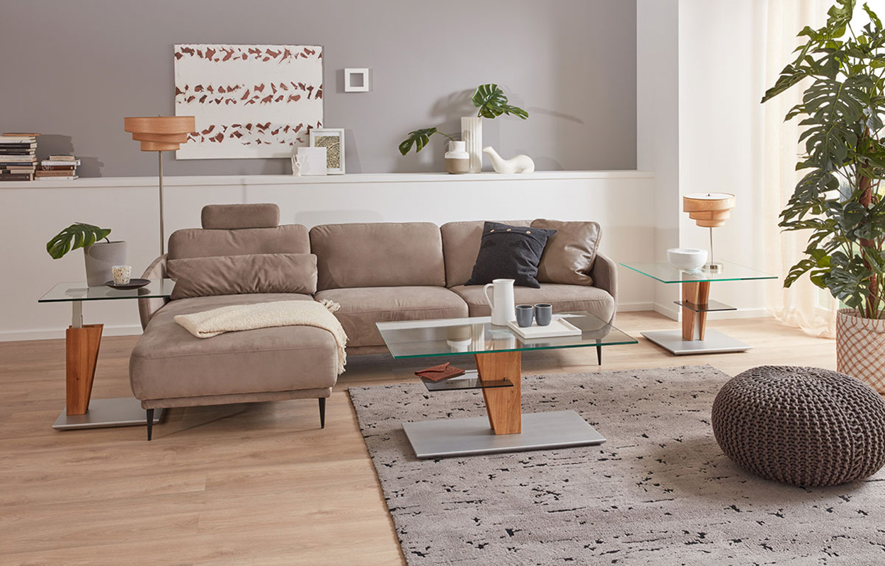 Couchtisch und zwei Beistelltische mit Glasplatten auf Holz- und Metallfüßen vor einem Sofa