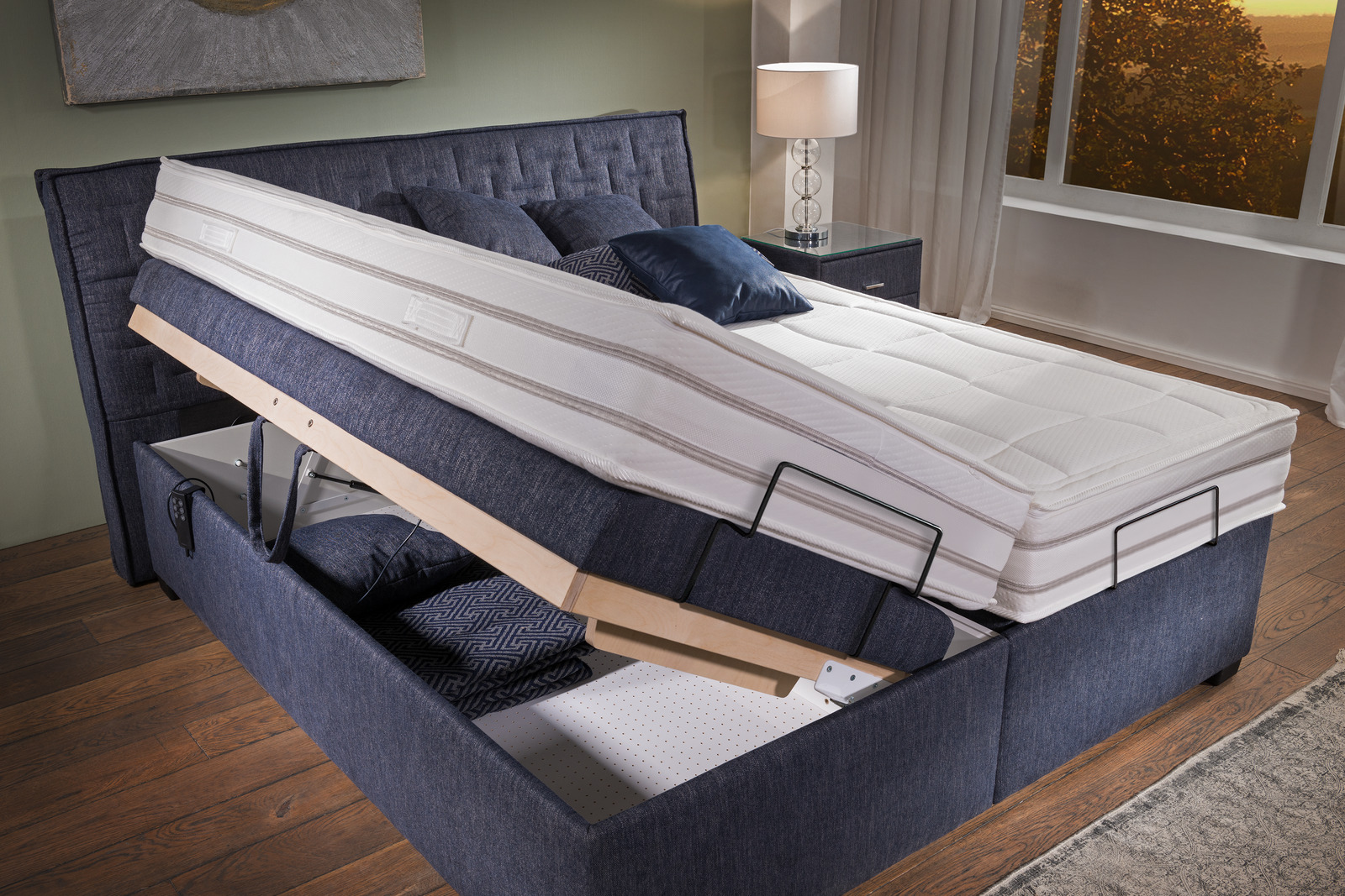 Blaues Bett mit hochgeklappter Liegefläche und sichtbarem Stauraum darunter