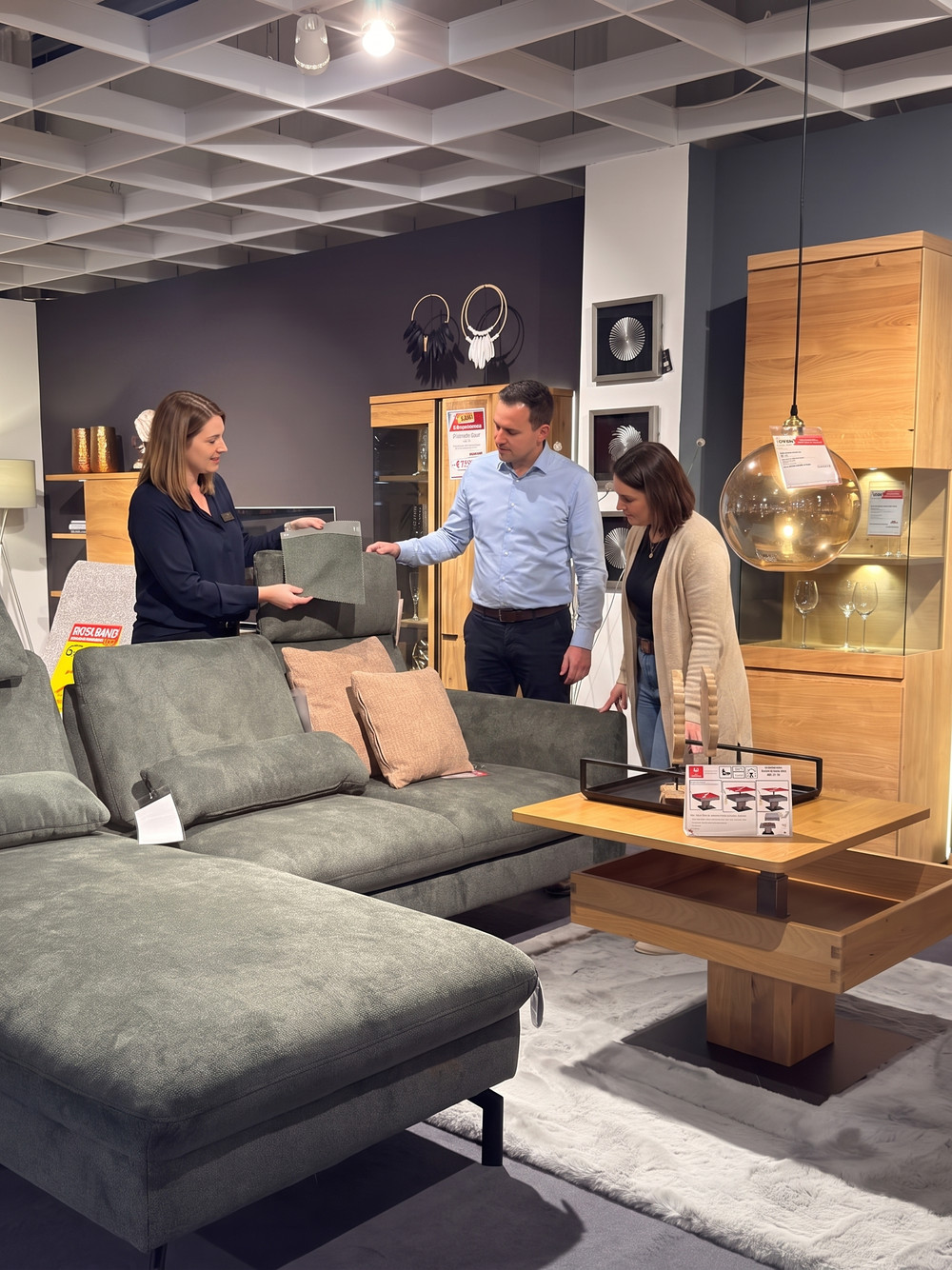 Verkäuferin zeigt einem Paar in der Ausstellung von Möbel Voigt ein Stoffmuster am Sofa